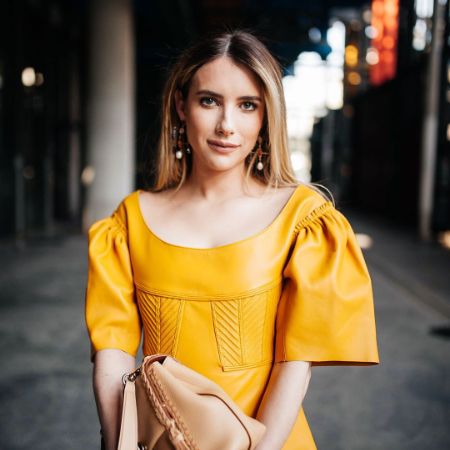 Emma Roberts is posing with a handbag wearing the yellow dress.